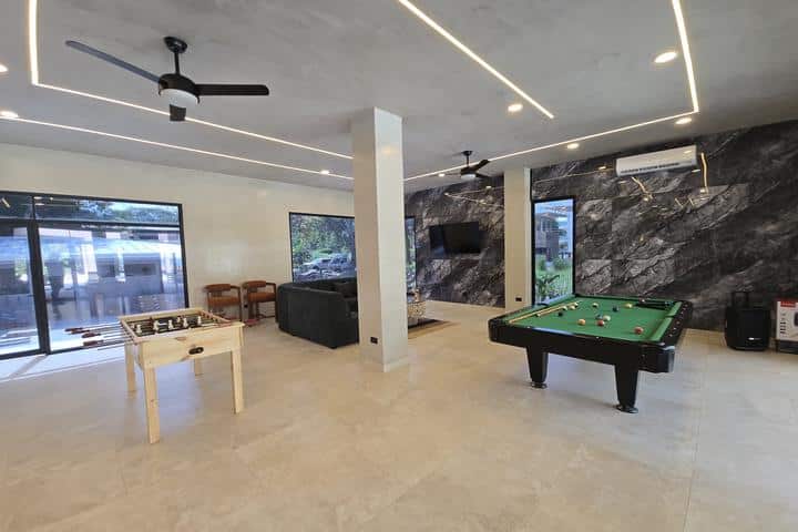 Spacious game room with a pool table, foosball table, and a black sofa near a marble wall. N/A lighting and ceiling fans above.