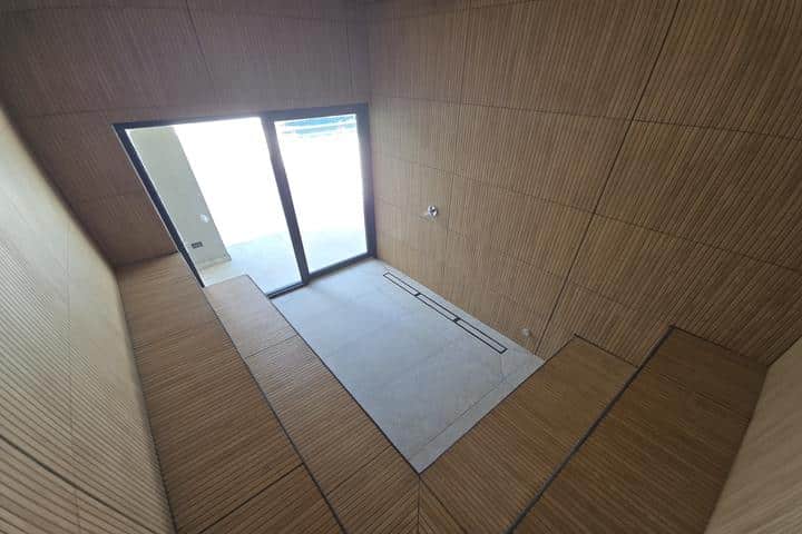 Modern interior entryway with wooden paneled walls and a glass door leading outside; sunken tile floor area at the entrance.