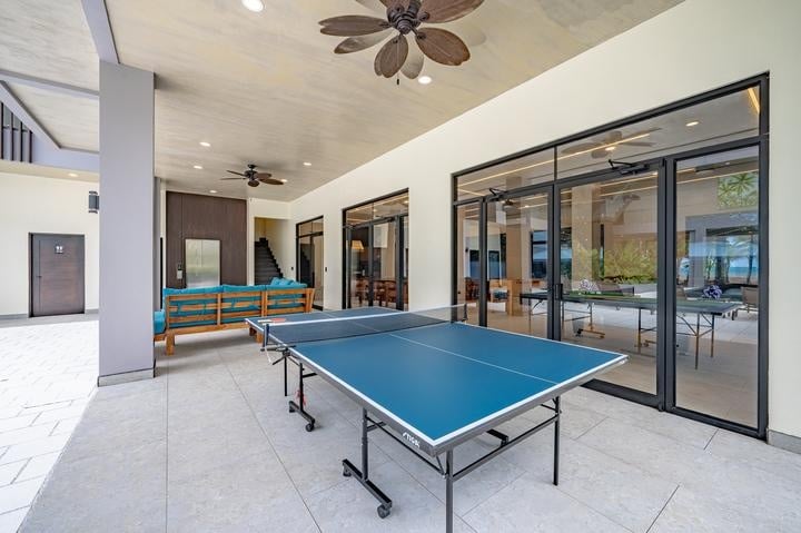 Beachfront Jaco, Costa Rica - Vacation Rental Casa Las Palmas • Costa Rica Elite Outdoor covered patio with a blue ping-pong table, ceiling fans, and teal seating beside glass-walled rooms.