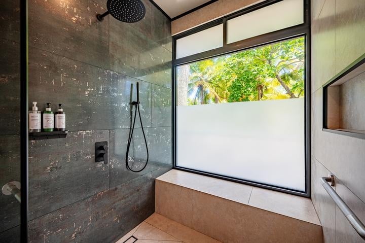 Beachfront Jaco, Costa Rica - Vacation Rental Casa Las Palmas • Costa Rica Elite Modern walk-in shower with dark stone tiles, a ceiling rainfall shower head and a handheld wand, next to a large frosted window overlooking green trees outside.