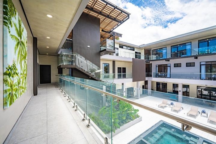 Beachfront Jaco, Costa Rica - Vacation Rental Casa Las Palmas • Costa Rica Elite Modern hotel atrium with glass railing overlooking a pool and balconies surrounding the courtyard.