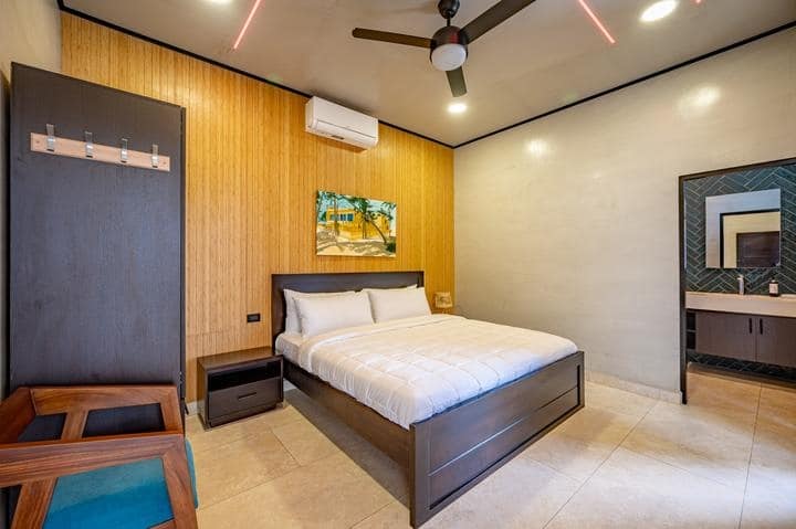 Beachfront Jaco, Costa Rica - Vacation Rental Casa Las Palmas • Costa Rica Elite Modern hotel room with a dark wood platform bed, white bedding, and two matching nightstands against a wood-paneled wall.