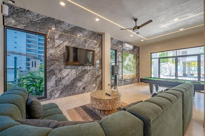 Beachfront Jaco, Costa Rica - Vacation Rental Casa Las Palmas • Costa Rica Elite Modern lounge area with green sectional sofa, marble wall with a mounted TV, and a round log coffee table