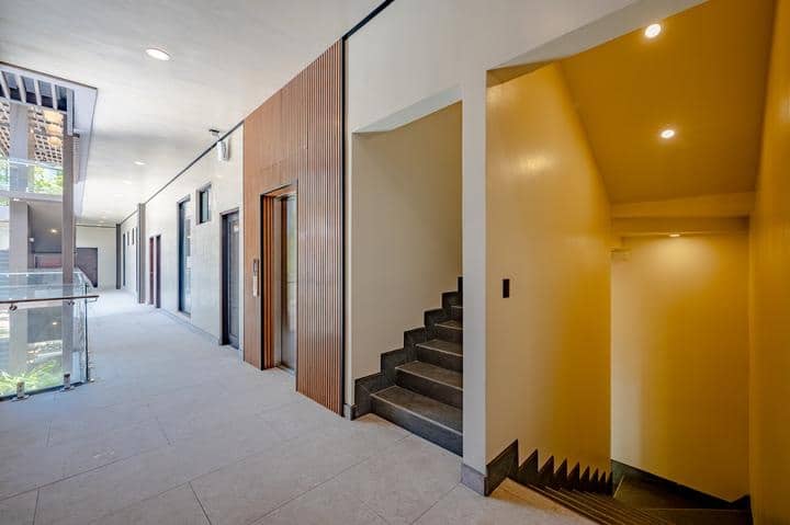 Beachfront Jaco, Costa Rica - Vacation Rental Casa Las Palmas • Costa Rica Elite Modern indoor hallway with elevator doors on the left and a yellow stairwell on the right, daylight at the far end.