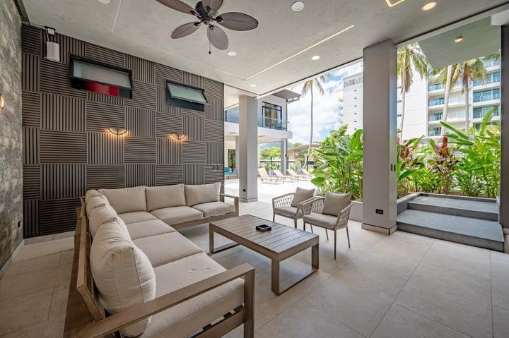 Beachfront Jaco, Costa Rica - Vacation Rental Casa Las Palmas • Costa Rica Elite Outdoor lounge with a beige sectional, coffee table, and wicker chairs under a ceiling fan by a poolside tropical garden.